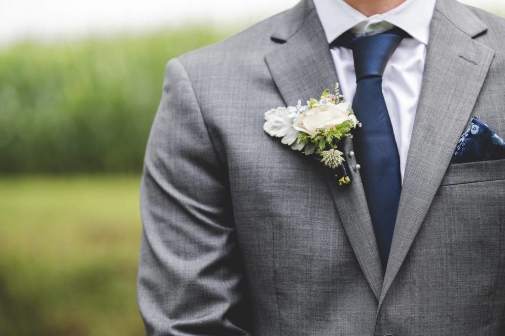 Homem vestido com um terno cinza com um buquezinho de flor na lapela do blazer