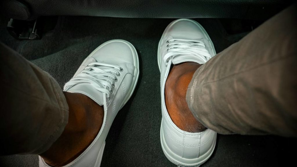 Foto está focando nos pés de uma pessoa com tênis brancos.
