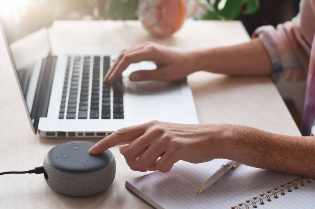 Moça trabalhando com um notebook e falando com a sua assistente virtual.