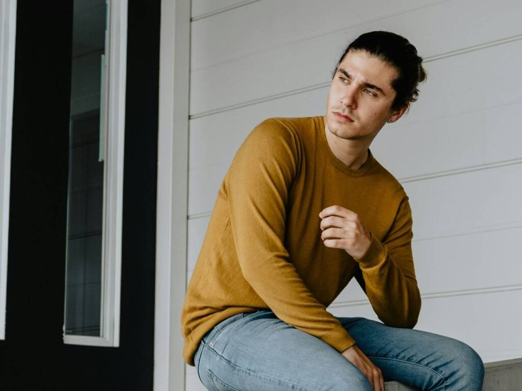 Homem sentando com camiseta da manga longa amarela.