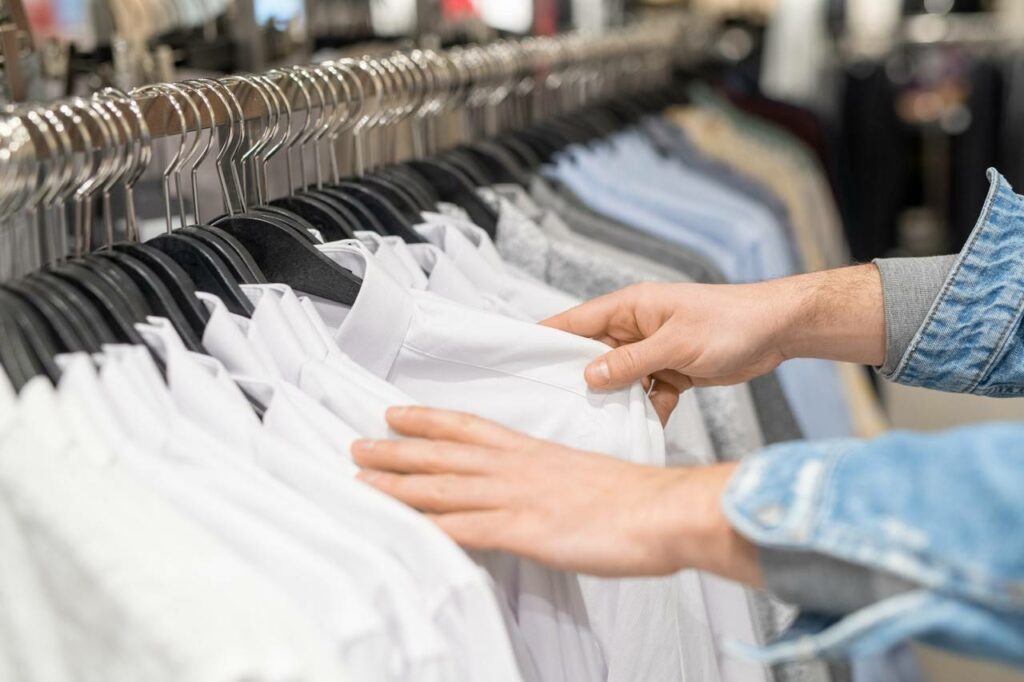 Pessoal olhando varia opções de camisa social em uma arara