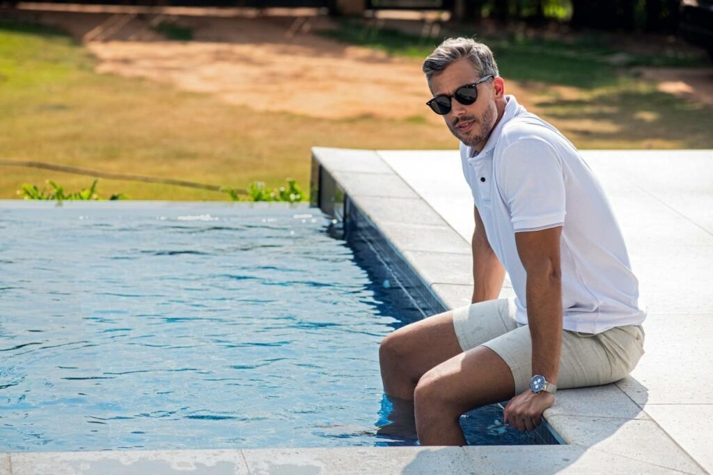 Homem sentado ma borda da piscina.