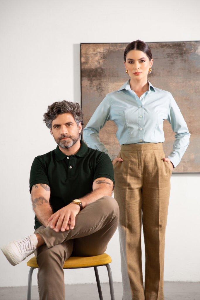 Homem com camisa polo preta sentado e mulher com camisa social azul clara em pé