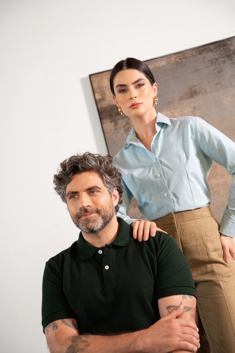 Homem com camisa polo verde escura e mulher com camisa social azul clara, uniformes corporativos
