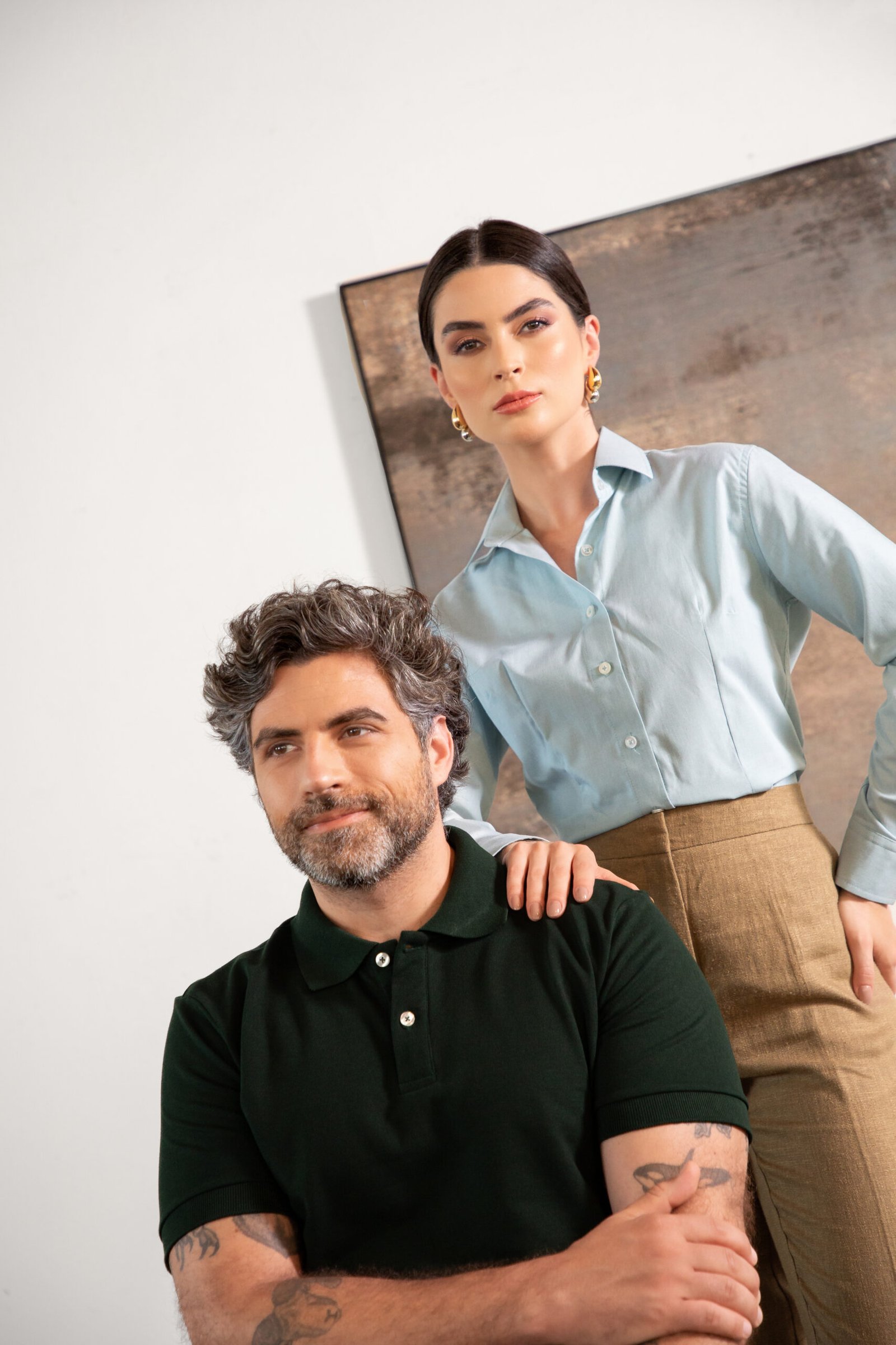 Homem com camisa polo verde escura e mulher com camisa social azul clara, uniformes corporativos