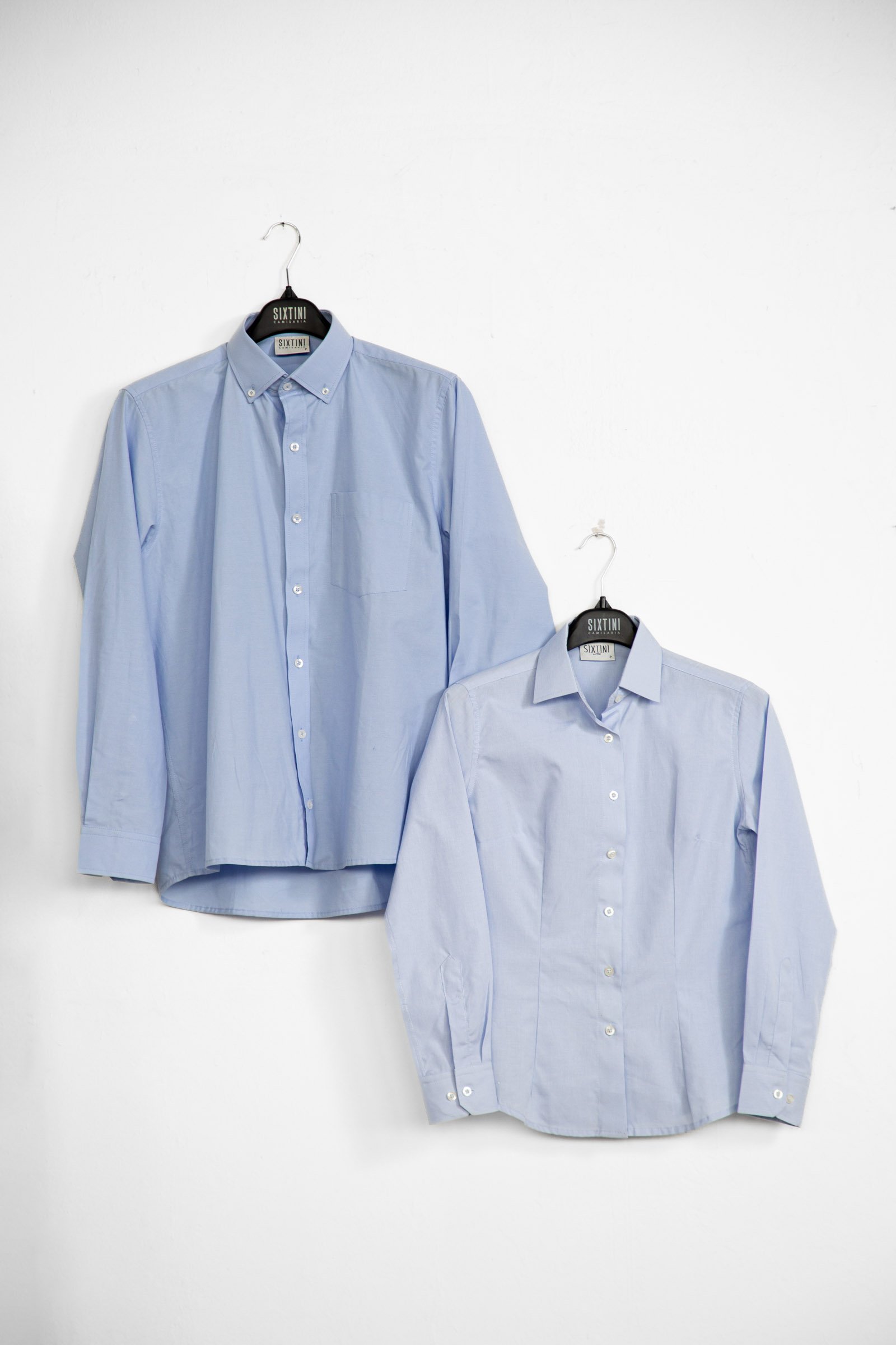 Duas camisas sociais azuis claras de manga longa penduradas em cabides