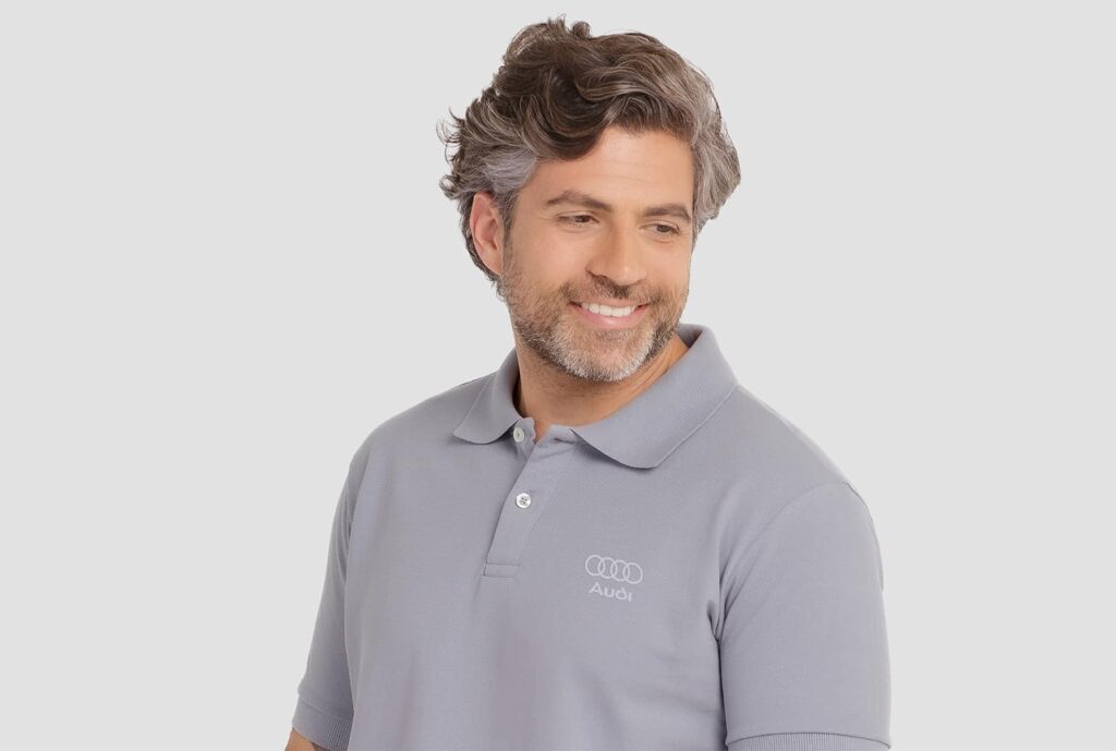 Homem vestindo camisa polo masculina cinza com logotipo Audi aplicado no lado esquerdo do peito.