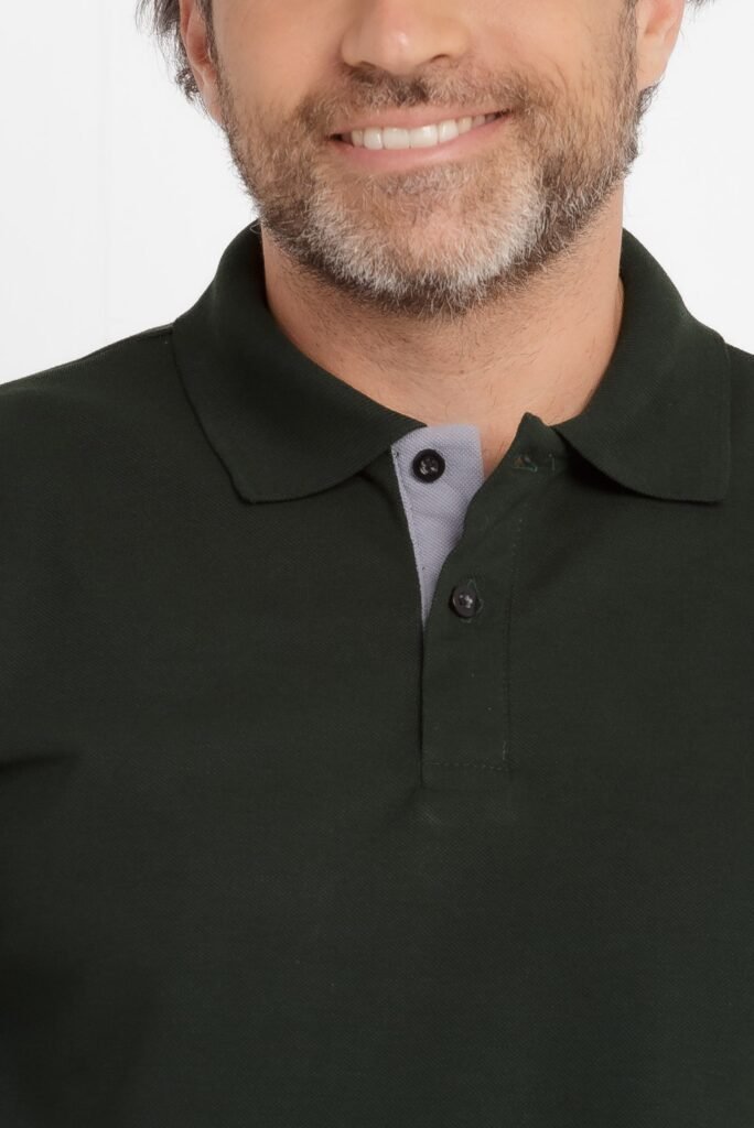 Close no tronco e no rosto inferior de um homem sorrindo, vestindo camisa polo verde escura com gola estruturada, vista interna em tom cinza claro e botões pretos. O tecido aparenta malha piquê de textura fina, com acabamento limpo e caimento ajustado, fundo branco de estúdio.