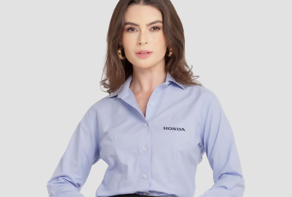 Mulher vestindo camisa social feminina azul clara com logotipo Honda aplicado no lado esquerdo do peito.