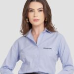 Mulher vestindo camisa social feminina azul clara com logotipo Honda aplicado no lado esquerdo do peito.