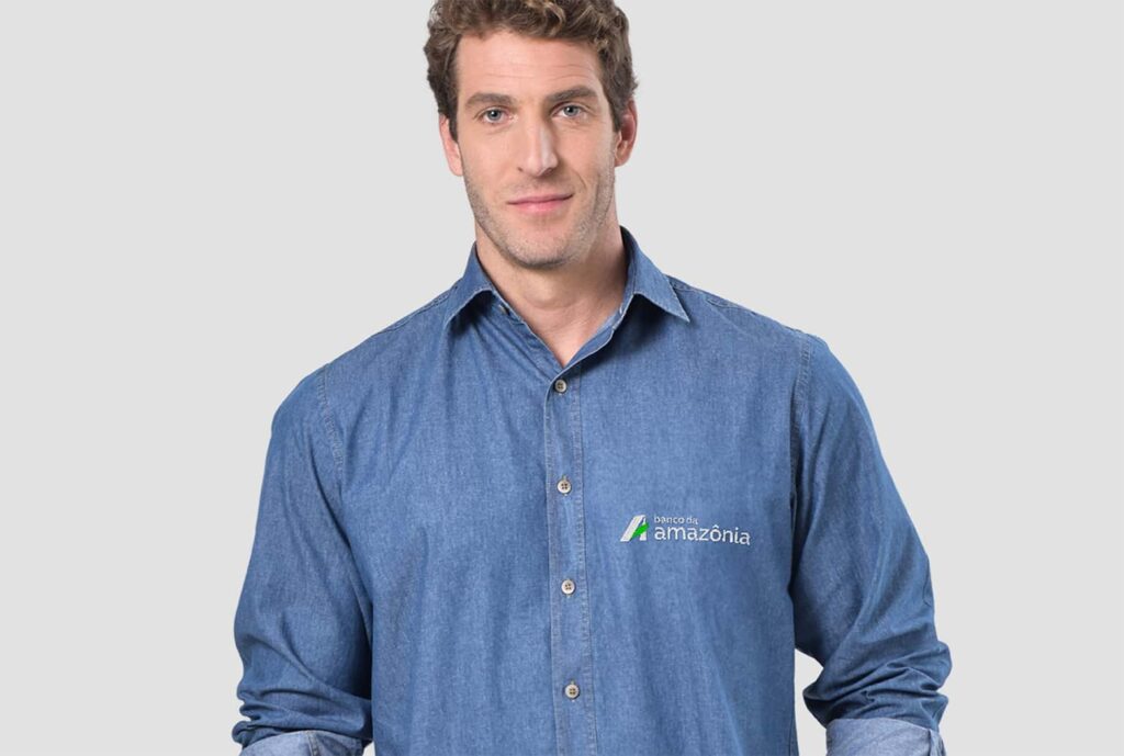 Homem vestindo camisa social masculina jeans com logotipo Banco da Amazônia aplicado no lado esquerdo do peito.