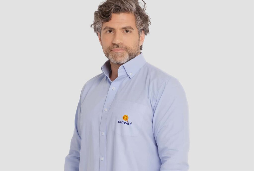 Homem vestindo camisa social masculina azul clara com logotipo Cutrale aplicado no lado esquerdo do peito.