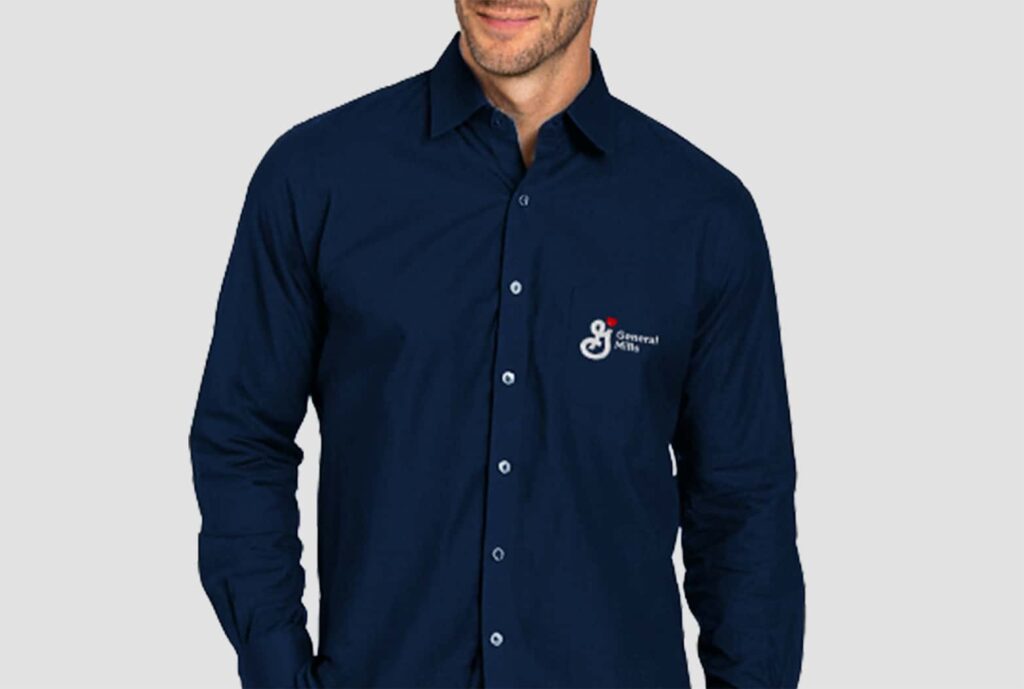 Homem vestindo camisa social masculina de manga longa na cor azul marinho, personalizada com logotipo General Mills bordado no lado esquerdo do peito.