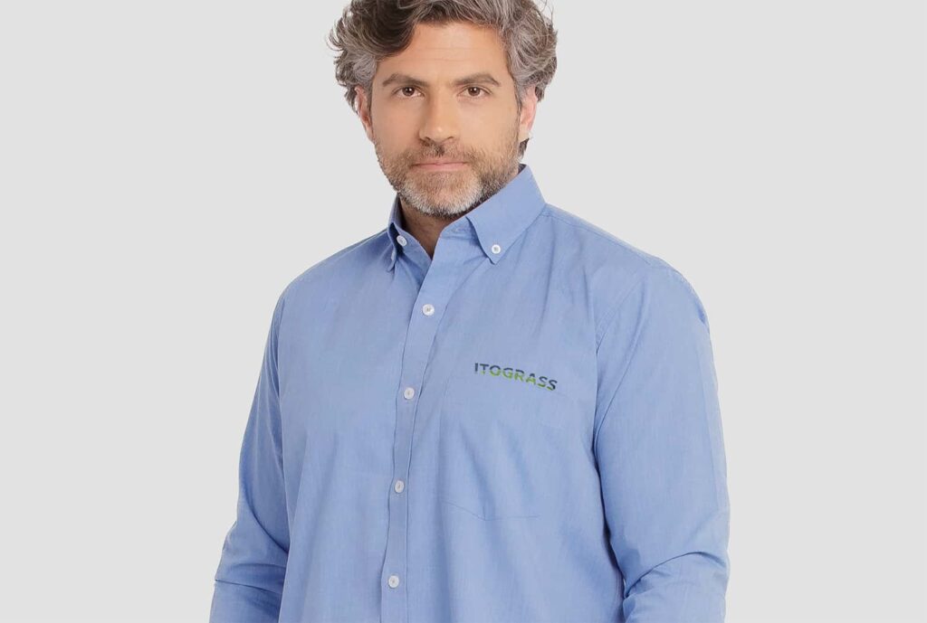 Homem vestindo camisa social masculina de manga longa na cor azul clara, com logotipo Itograss bordado no lado esquerdo do peito.