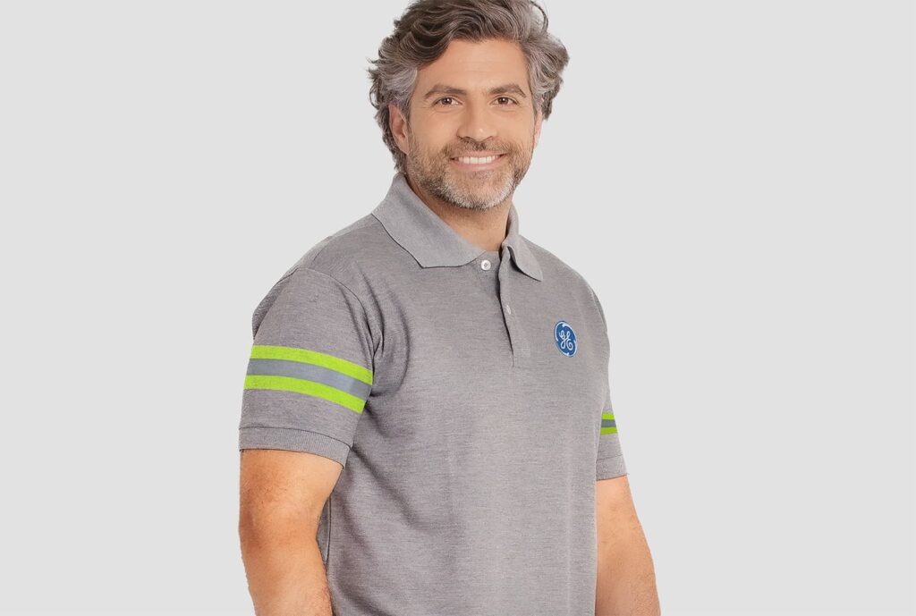 Homem vestindo camisa polo masculina cinza com logotipo GE aplicado no lado esquerdo do peito e faixas refletivas verde neon nas mangas.