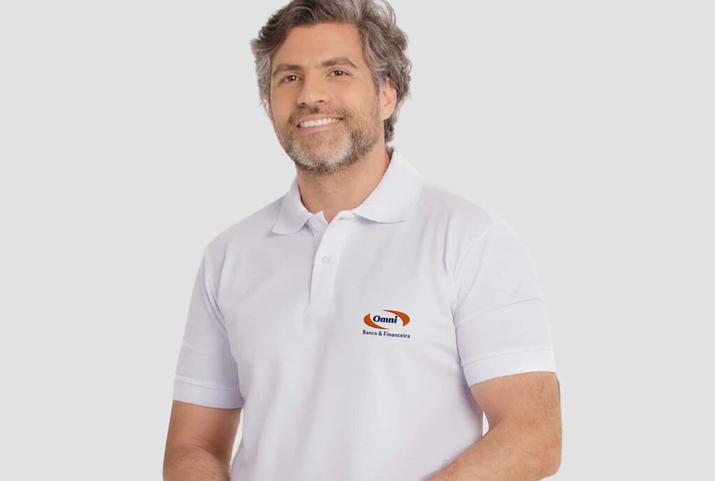 Homem vestindo camisa polo masculina branca, com logotipo Omni Banco & Financeira aplicado no lado esquerdo do peito.