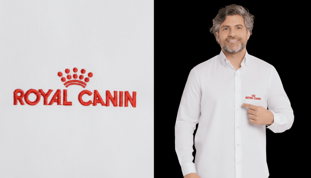 Imagem composta por dois enquadramentos da camisa social corporativa branca personalizada Royal Canin. À esquerda, close-up do bordado “ROYAL CANIN” em vermelho com o símbolo de coroa acima do nome, aplicado sobre tecido branco de textura fina. À direita, modelo masculino vestindo camisa social branca de manga longa, com colarinho estruturado e fechamento por botões, apontando para o bordado Royal Canin em vermelho no lado esquerdo do peito. A peça apresenta modelagem profissional e acabamento refinado.