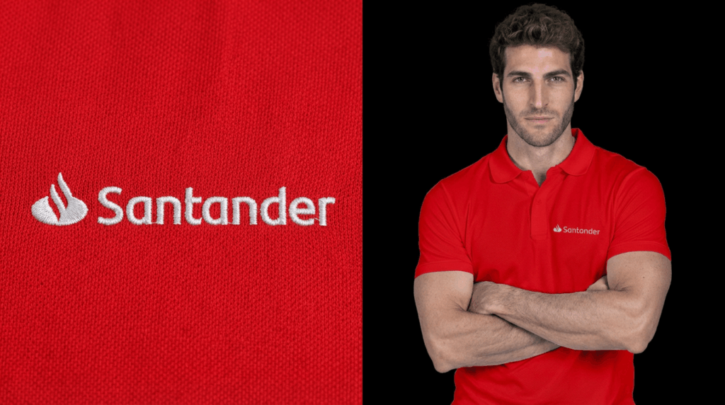 Imagem em close do bordado Santander em linha branca aplicado sobre camisa polo vermelha, ao lado de modelo masculino vestindo polo vermelha com o logotipo bordado no peito e braços cruzados.