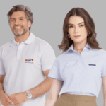 Dois modelos em fundo neutro cinza vestindo uniformes corporativos personalizados. À esquerda, modelo masculino usando polo branca com gola estruturada e fechamento por botões, bordada no lado esquerdo do peito com o logo “Omni Banco & Financeira” em azul e laranja. À direita, modelo feminina vestindo camisa social azul clara de manga curta, com colarinho clássico e fechamento por botões frontais, bordada no lado esquerdo do peito com o logo “CASIO” em azul marinho. As peças apresentam modelagem profissional, excelente caimento e bordado empresarial de alta definição.