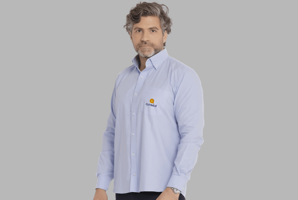 Homem vestindo camisa social masculina azul clara com logotipo Cutrale aplicado no lado esquerdo do peito.
