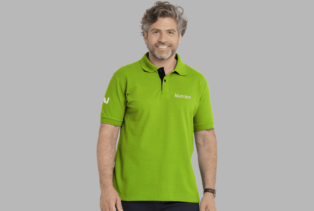 Homem vestindo camisa polo masculina verde com logotipo Nutrien aplicado no lado esquerdo do peito e detalhe na manga.