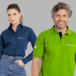 Dois modelos em fundo neutro cinza vestindo uniformes corporativos personalizados. À esquerda, modelo feminina usando camisa social azul marinho de manga longa, com colarinho estruturado e fechamento por botões frontais, bordada no lado esquerdo do peito com o logo “Ourofino Saúde Animal” em branco. A camisa está combinada com jeans, mas o destaque é a peça superior personalizada. À direita, modelo masculino vestindo polo verde vibrante com gola estruturada e carcela com botões escuros, bordada no lado esquerdo do peito com o logo “Nutrien” em branco e detalhe adicional na manga. Ambas as peças apresentam acabamento refinado, modelagem profissional e bordado de alta definição.