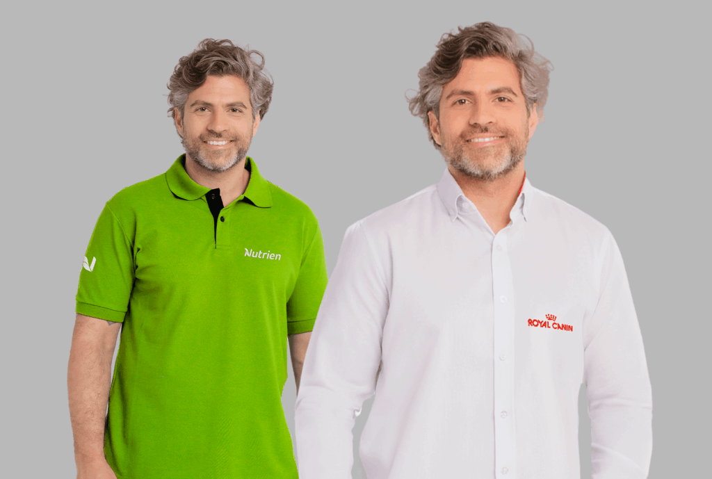 Dois modelos masculinos em fundo neutro cinza vestindo uniformes corporativos personalizados. À esquerda, polo verde vibrante com gola estruturada e carcela com botões escuros, bordada no lado esquerdo do peito com o logo “Nutrien” em branco e detalhe adicional na manga. À direita, camisa social branca de manga longa com fechamento por botões e colarinho estruturado, bordada no lado esquerdo do peito com o logo “Royal Canin” em vermelho. As peças apresentam modelagem profissional, acabamento refinado e bordado de alta definição, ideais para padronização empresarial.