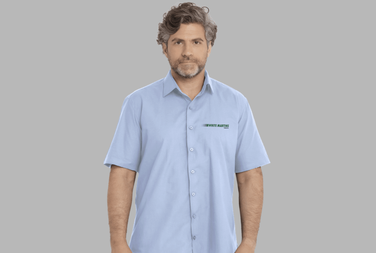 Homem vestindo camisa social masculina azul claro de manga curta com bordado White Martins aplicado no lado esquerdo do peito.